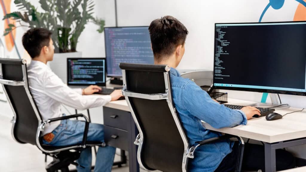 Dva studenti programují v jazyce Java na počítačích v učebně.