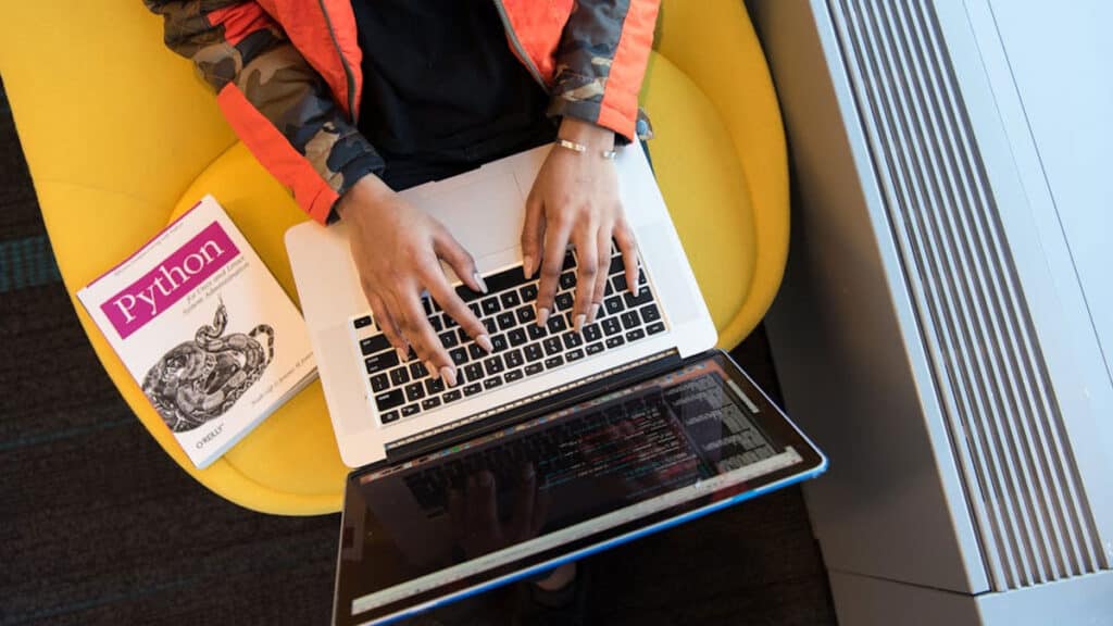 Studentka se učí Python s notebookem a knihou během online kurzu programování.